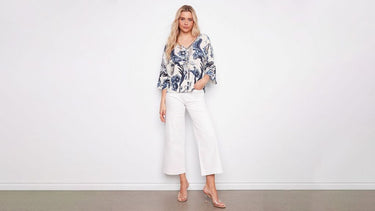 Woman wearing a blue and white paisley print blouse with cropped white wide-leg jeans and clear heeled sandals.