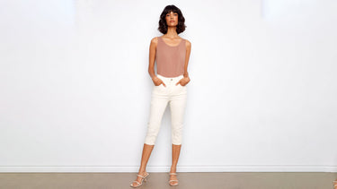 A woman wears the best capri pants for women in white denim, styled with a mauve tank top and nude heeled sandals