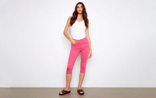 A woman wears pink capri pants styled with a white tank top and dark brown buckle slide sandals.