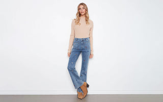 A woman wearing a beige sweater with heart-embroidered flare jeans