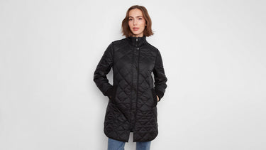 A woman wearing a black quilted jacket with knit cuffs and jeans.
