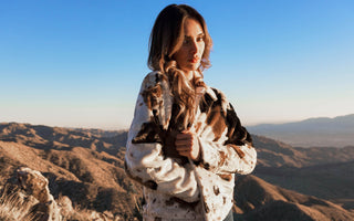 A woman wearing a spotted faux fur jacket in the desert mountains.