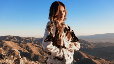 A woman wearing a spotted faux fur jacket in the desert mountains.
