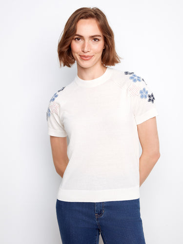 White cotton knit top with intricate floral embroidery on the sleeves and a comfortable crew neckline by Charlie B.