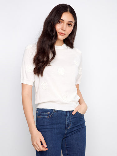 Cotton knit top in white showcasing elegant floral applique and crew neckline, worn with jeans by Charlie B.