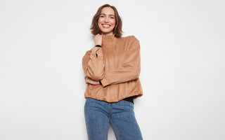 Woman wearing a camel suede bomber jacket over a black top, paired with medium-wash jeans.