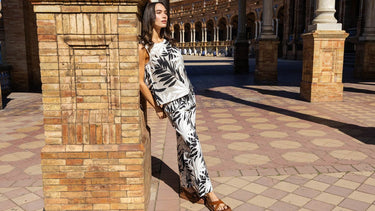 A woman wearing a black and white palm leaf print sleeveless top and matching wide-leg pants, photographed outdoors in full length.