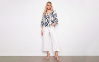  Woman wearing a blue and white paisley print blouse with cropped white wide-leg jeans and clear heeled sandals.