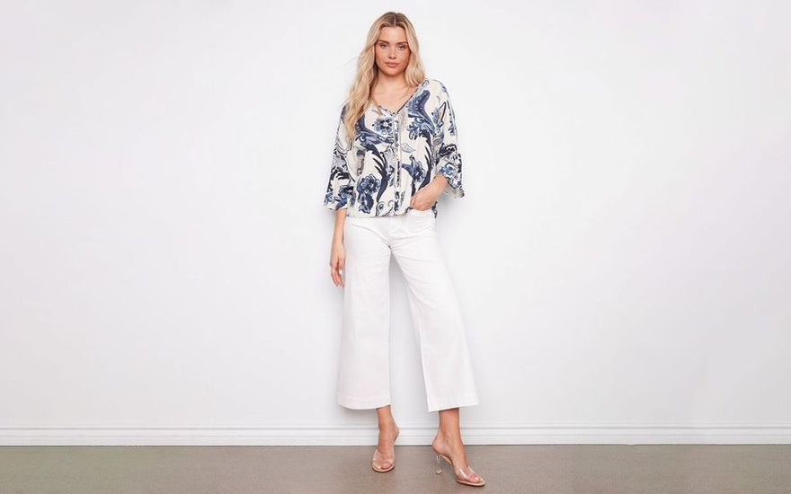  Woman wearing a blue and white paisley print blouse with cropped white wide-leg jeans and clear heeled sandals.