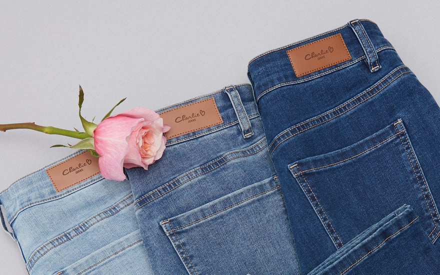 Pair of Charlie B blue jeans with a pink rose on a light gray background