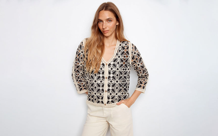 A woman wears a black and off-white crochet cardigan.