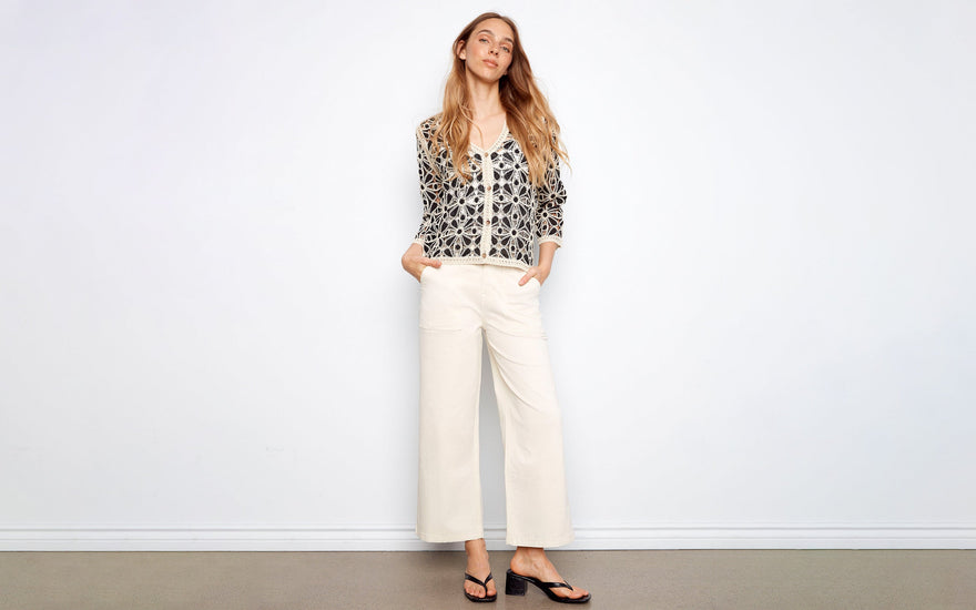 A woman wears a crochet cardigan outfit idea with cream wide-leg pants, black sandals, and a V-neck button front.