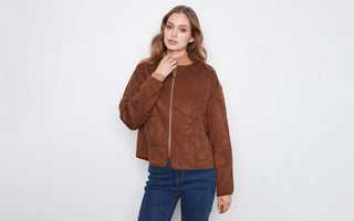  Woman wearing a brown floral embroidered suede jacket over a camel turtleneck, paired with dark wash jeans.