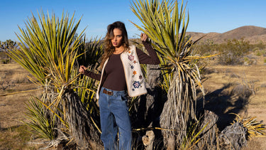 A woman wearing a floral-embroidered vest with jeans in the desert 