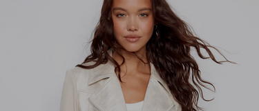 A woman with wavy brown hair wearing a cream suede jacket.
