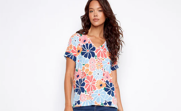 A woman wearing a V-neck top in a bold retro floral print with mid-wash bootcut jeans and brown block heel sandals.
