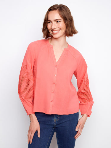 This coral blouse showcases intricate embroidery on the sleeves, creating an eye-catching design. By Charlie B.