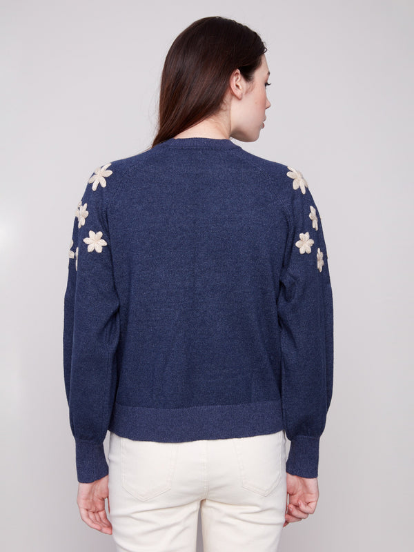 Chic heather denim sweater adorned with delicate white floral embroidery on the shoulders, highlighting its raglan puff sleeves by Charlie B.