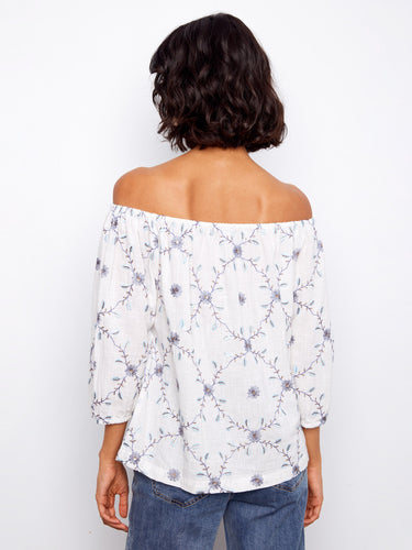 Graceful off-the-shoulder blouse adorned with delicate floral details on premium 100% cotton fabric. A timeless piece by Charlie B.