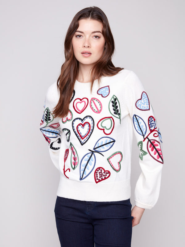 Ecru sweater adorned with colorful embroidery of hearts and leaves, showcasing a relaxed fit design by Charlie B.