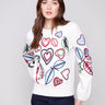 Ecru sweater adorned with colorful embroidery of hearts and leaves, showcasing a relaxed fit design by Charlie B.