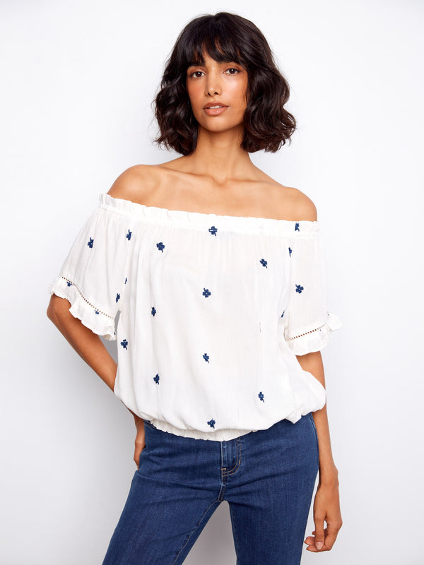 White blouse with blue embroidered flowers and short flutter sleeves, featuring an elastic hem by Charlie B.