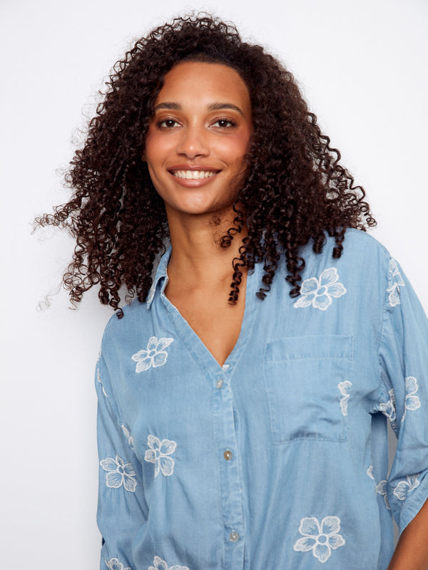 Light blue blouse showcasing a chest pocket and floral embroidery, complete with button closure by Charlie B.