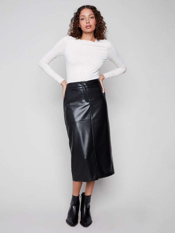 Black faux leather midi skirt with convenient side pockets, paired elegantly with a white top and black ankle boots by Charlie B.