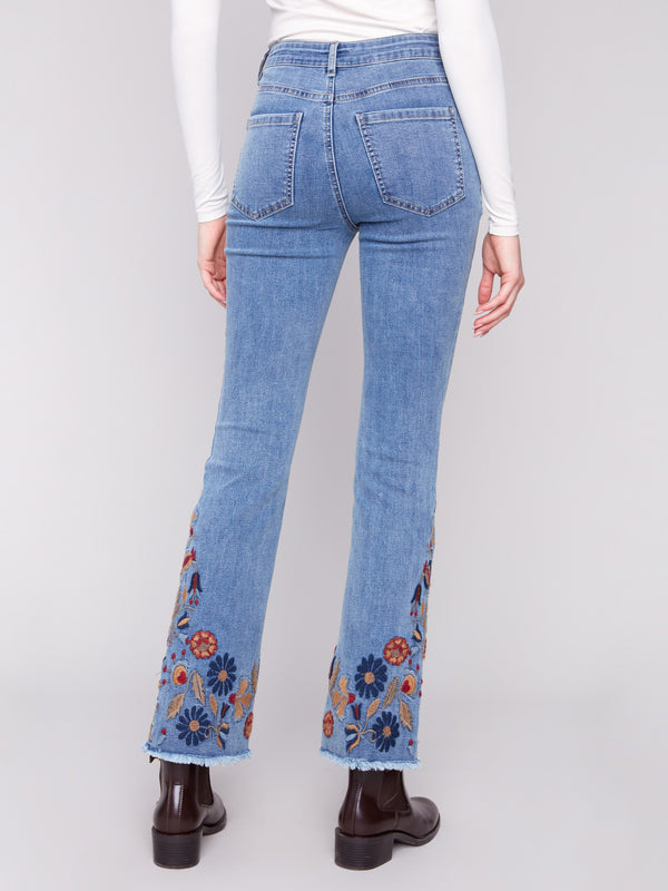 Medium blue jeans showcasing a classic five-pocket design and detailed colorful embroidery at the hem by Charlie B.