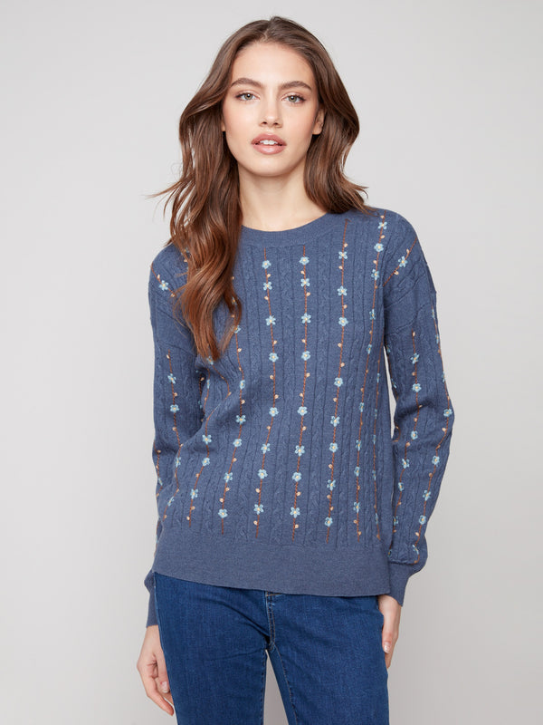 Elegant tulip knit sweater showcasing intricate cable plush design and ribbed cuffs, paired with floral embroidery by Charlie B.