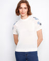 White cotton knit top with intricate floral embroidery on the sleeves and a comfortable crew neckline by Charlie B.
