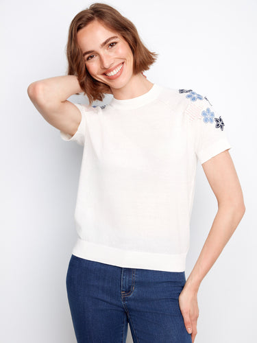 This stylish white cotton top features raglan short sleeves adorned with delicate floral appliques by Charlie B.