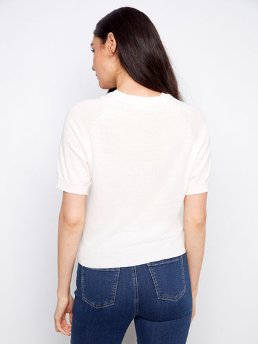 White cotton knit top highlighting its raglan sleeves and crew neck design, complemented by blue jeans by Charlie B.