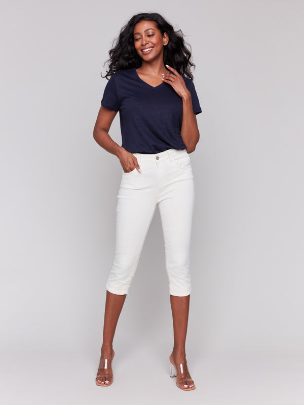 Woman in a navy short-sleeve top and natural knee-high capri pants, posing against a light gray background in clear high-heel sandals.