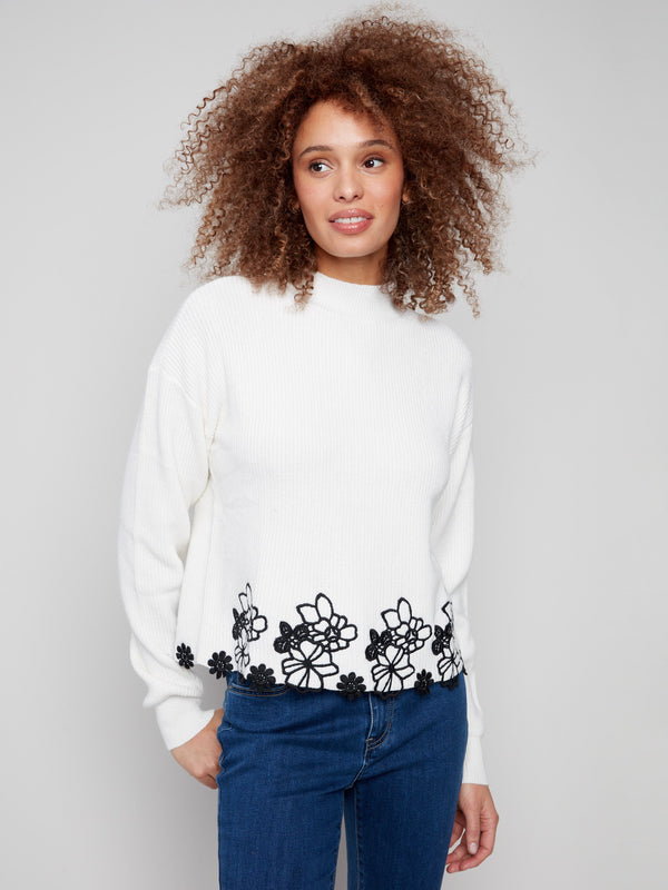 Ecru sweater featuring a mock neck and intricate black floral lace hem, showcasing a drop shoulder design by Charlie B.