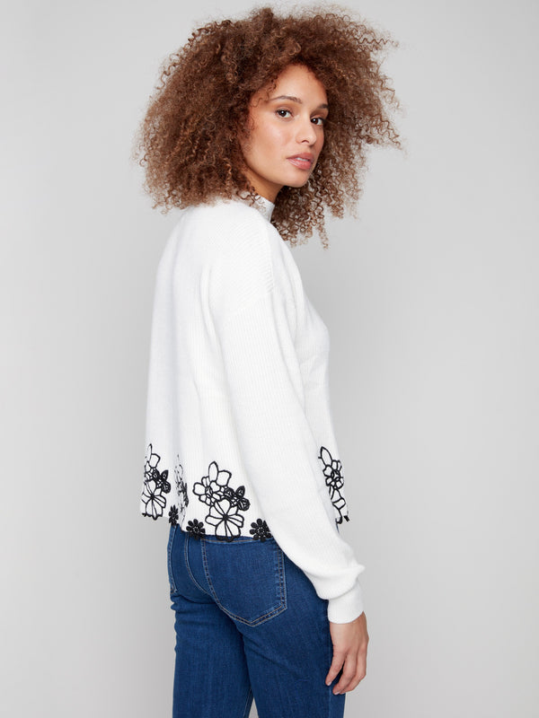 Sophisticated ecru sweater featuring hip-length cut and elegant black floral lace trim for added flair by Charlie B.