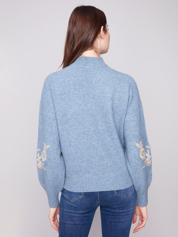 Stylish heather denim piece highlighted by intricate embroidered flowers and drop shoulder design by Charlie B.