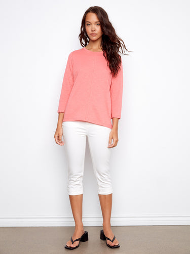 Stylish coral top featuring front seam detail, matched with crisp white pants for a chic look. By Charlie B.