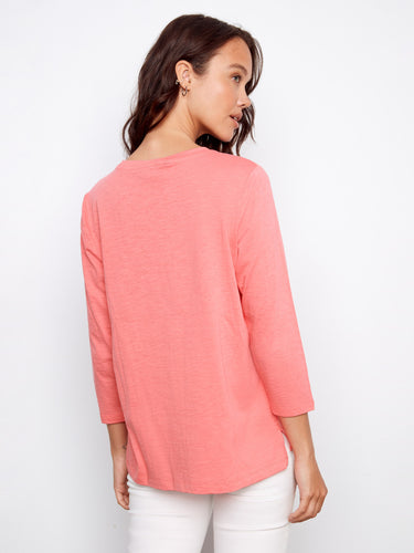 Casual coral top with a slit hem, adding subtle flair to your outfit when worn with white bottoms. Crafted by Charlie B.