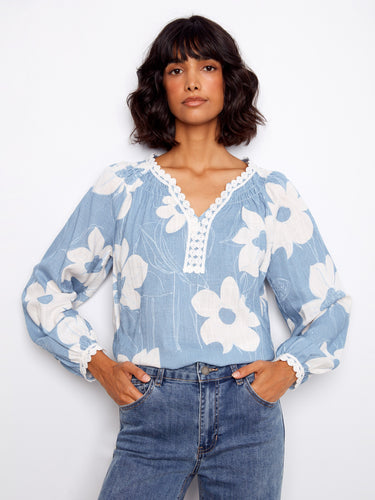 Soft blue blouse adorned with intricate crochet trim on cuffs, enhancing its feminine appeal and style by Charlie B.