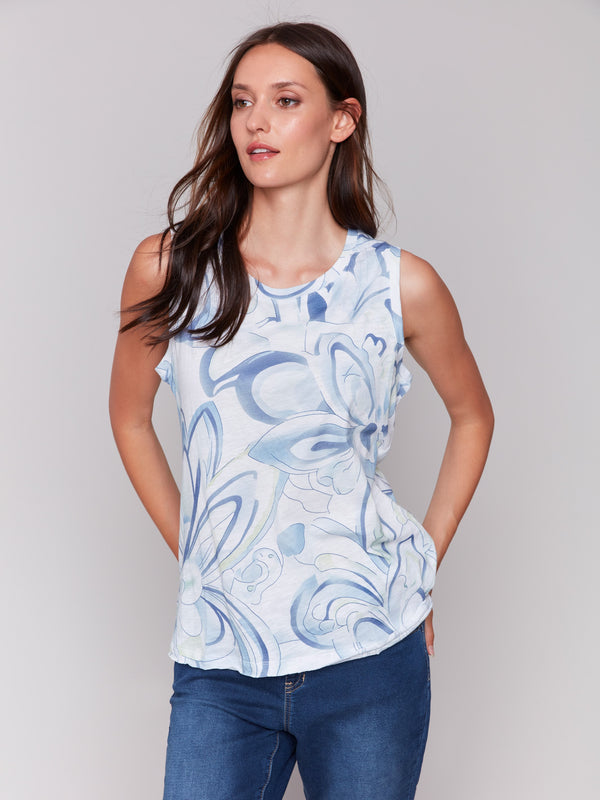 Woman in a blue and white swirl print sleeveless top and blue jeans, posing against a light gray background.